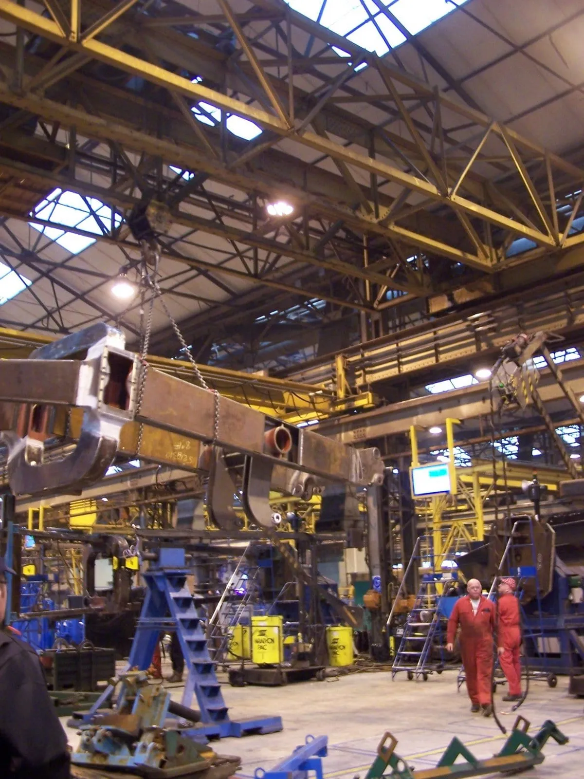 A heavy truck frame hanging from a crane in a fabrication hall