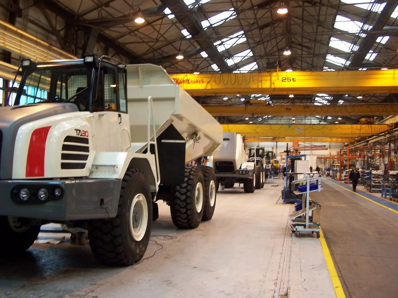 A white TA30 articulated haul truck on a factory floor under yellow cranes
